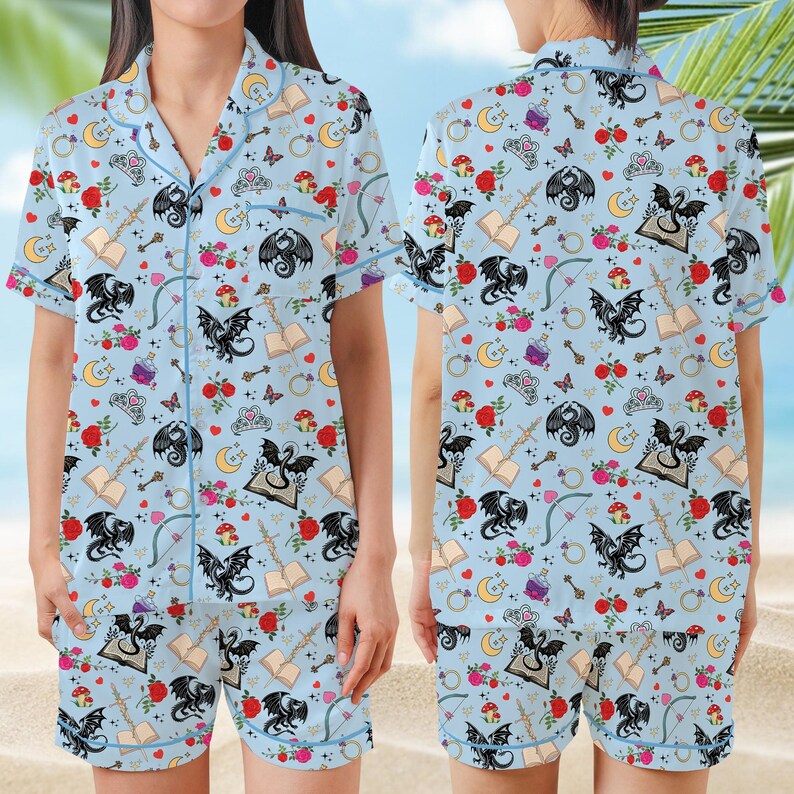 K&ouml;nnte beinhalten: Hellblaues Pyjama-Set mit einem fantasievollen Muster aus schwarzen Drachen, Rosen und B&uuml;chern. Das kurz&auml;rmelige Oberteil und die Shorts haben blaue Paspeln. Der Stoff ist weich und leicht.