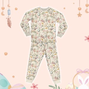May include: Cream-coloured two-piece pyjama set with a floral and egg pattern. The long-sleeved top and trousers have a relaxed fit with ribbed cuffs and a crew neck. The design features pastel-coloured flowers and Easter eggs, perfect for a cosy night.