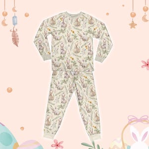 May include: A cream-coloured two-piece pyjama set with a repeating pattern of watercolour bunnies and foliage. The long-sleeved top and trousers have light grey trim. The pyjamas are designed for comfort and sleep.