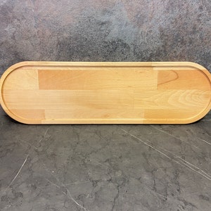 Puede incluir: Una bandeja de servir de madera larga y ovalada con un acabado de madera natural. La bandeja está hecha de madera clara y tiene una superficie lisa.