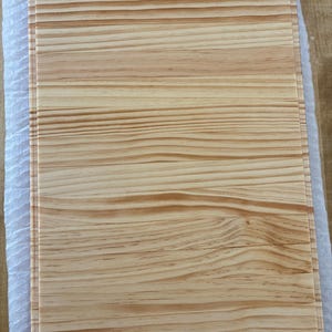 Può includere: Un tagliere rettangolare in legno di colore marrone chiaro con evidenti venature orizzontali. Il tagliere presenta una superficie liscia e piatta con bordi dritti, che mettono in risalto la consistenza naturale e le variazioni del legno.