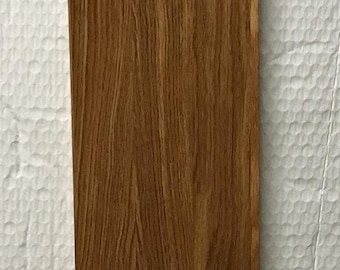 May include: A rectangular piece of wood with a rich, brown color and prominent wood grain. The wood grain pattern is vertical, creating a natural and textured appearance. The wood appears to be a solid plank.