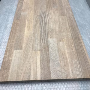 Puede incluir: Una mesa rectangular de madera con un acabado marrón claro. La veta de la madera es visible y la superficie está hecha de múltiples tablones unidos. La mesa es probablemente para un escritorio o mesa.