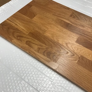 May include: A rectangular wooden tabletop with a natural oak finish. The wood grain is visible, and the surface is composed of multiple planks. The tabletop is resting on a white, bubble-wrap surface.
