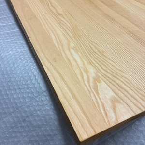 May include: A rectangular wooden tabletop with a light, natural wood grain finish. The wood grain pattern is visible across the surface. The edges of the tabletop are finished with a darker wood trim. The tabletop is likely for a desk or table.
