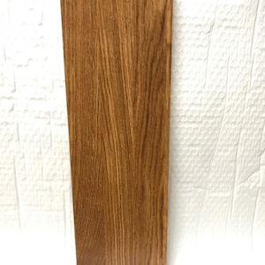 May include: A close-up of a wooden board with a natural wood grain finish. The board is light brown in color and has a smooth surface.
