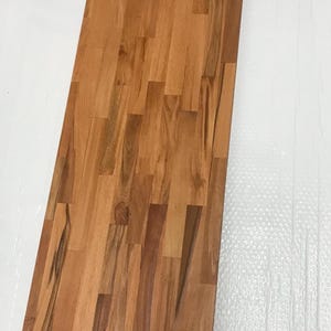 Könnte beinhalten: Ein langes, rechteckiges Holzbrett aus mehreren Holzstücken, die in einem Parkettmuster angeordnet sind. Das Holz ist hellbraun mit einigen dunkleren braunen Streifen.