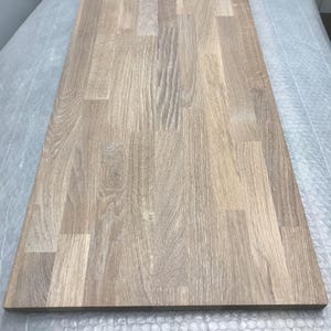 May include: A rectangular wooden tabletop with a light brown finish. The wood grain is visible, and the surface is made of multiple planks joined together. The tabletop is likely for a desk or table.