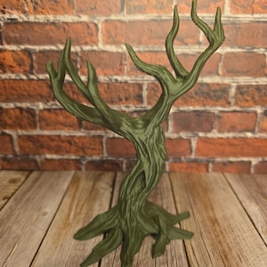 May include: A dark green, stylized tree sculpture with a textured trunk and branches. The sculpture has a detailed, organic design, resembling a miniature tree. The base is spread out, and the branches reach upwards. The background features a brick wall and wooden planks.