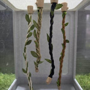 May include: Four decorative hanging vines with braided rope and faux leaves. The vines are in various colours: white, tan, black, and brown. Each vine has a wooden top and bottom.