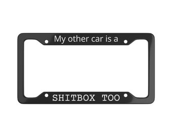 以下が含まれることがあります： 「My other car is a SHITBOX TOO」というテキストが書かれた黒いナンバープレートフレーム。