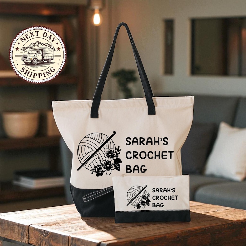 A white tote bag with black handles and a smaller bag with a similar design, both featuring the text "SARAH'S CROCHET BAG" and a crochet hook graphic. The bag is placed on a wooden table, and there is a couch and a lamp in the background.