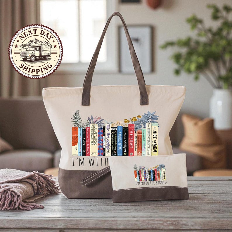 A beige tote bag with a printed design of colorful books and the text "I'm with the Banned" printed on it, along with a smaller bag or pouch with the same design.