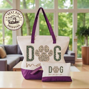 A large tote bag with a leopard print paw print design and the word "dog" printed on it, along with a smaller bag that says "dog mama" on it. The bags are placed on a wooden surface, and there is a window and a couch in the background.