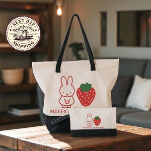 a white tote bag with a cartoon rabbit and a strawberry, along with a smaller bag that also has a cartoon rabbit and a strawberry on it, placed on a wooden table.