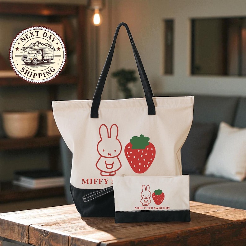 a white tote bag with a cartoon rabbit and a strawberry, along with a smaller bag that also has a cartoon rabbit and a strawberry on it, placed on a wooden table.