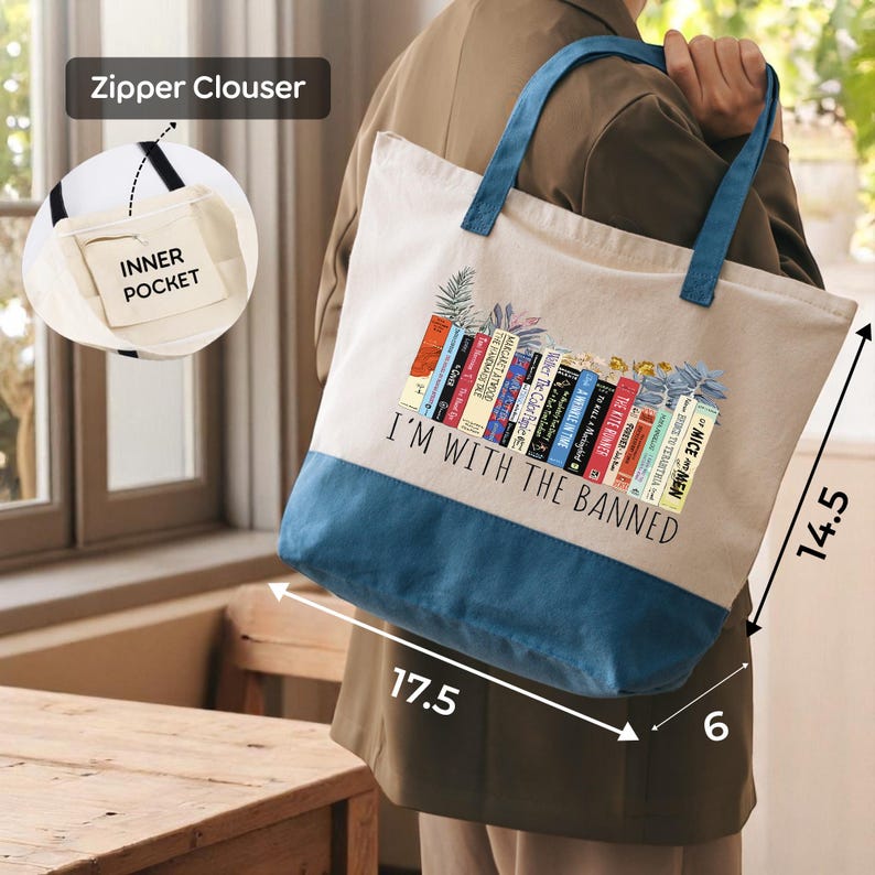 A person is holding a tote bag with a printed design of colorful books and the text "I'm with the Banned" printed on it.