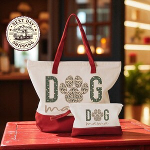 A red and white tote bag with the word "dog" printed on it, along with a smaller bag that says "dog mama" on it, placed on a red surface.