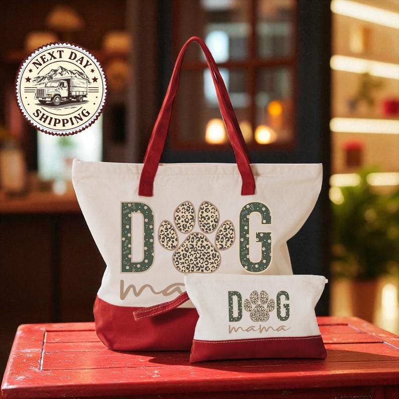 A red and white tote bag with the word "dog" printed on it, along with a smaller bag that says "dog mama" on it, placed on a red surface.