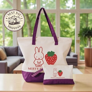a large tote bag and a smaller pouch with a cartoon rabbit design, both with a strawberry motif, placed on a wooden surface.