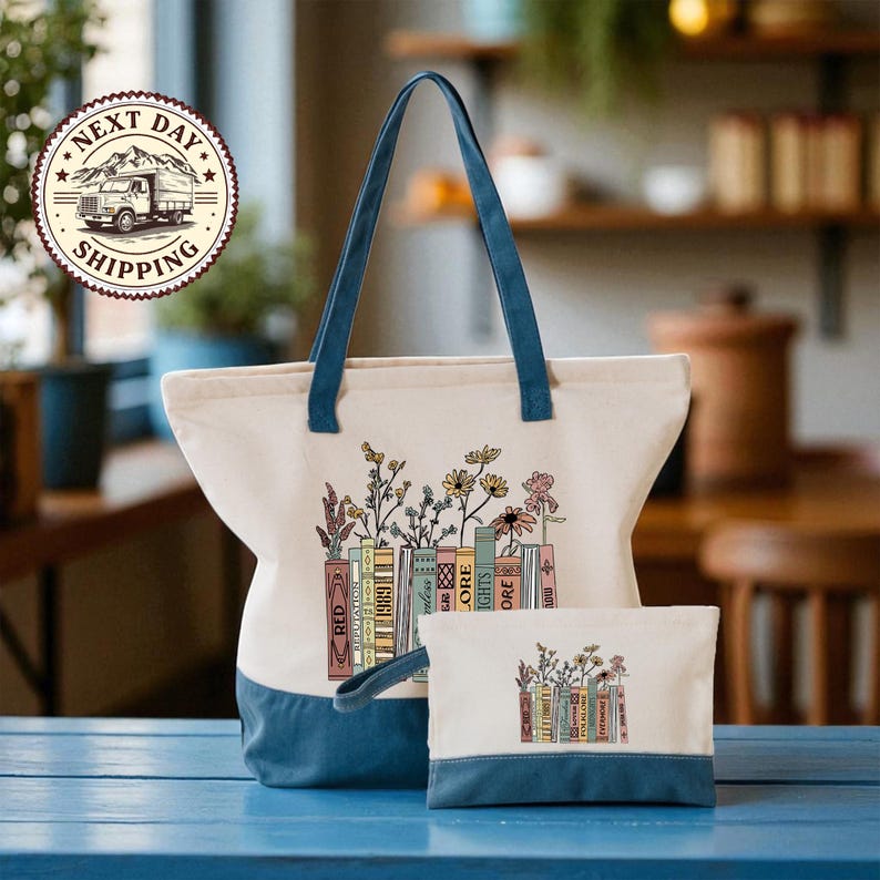 A large tote bag with a printed design of books and flowers, and a smaller bag with a similar design, both sitting on a blue surface.