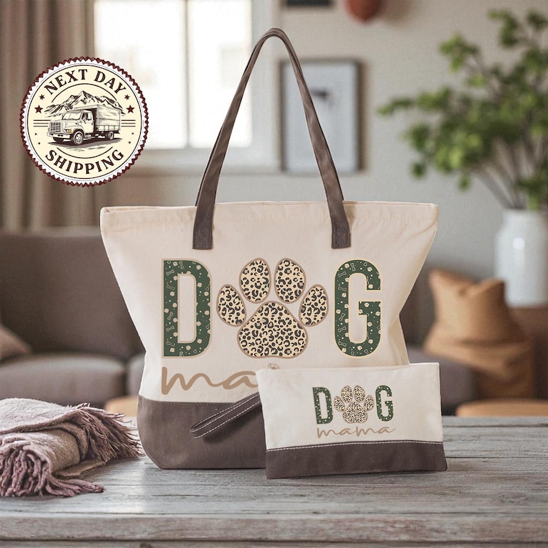 A beige tote bag with a leopard print paw print design and the word "dog" printed on it, along with a smaller bag that says "dog mama" on it. The bag is placed on a wooden surface, and there is a potted plant in the background.