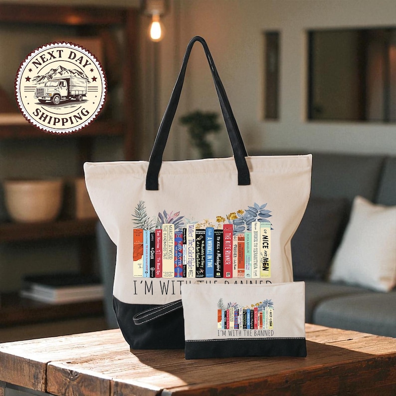 A white tote bag with a printed design of colorful books and the text "I'm with the Banned" printed on it, placed on a wooden table.