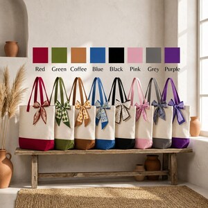 A row of colorful tote bags with bows, each with a different color, displayed on a wooden bench against a white wall.
