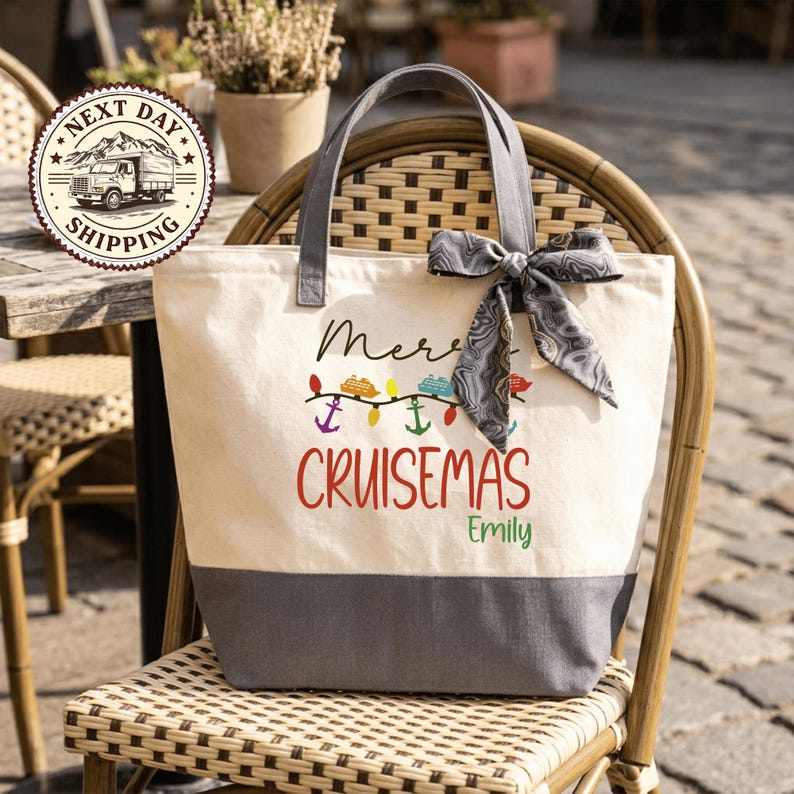 A beige tote bag with a gray handle and a gray ribbon tied around it, sitting on a wicker chair. The bag has a printed design that says "Merry Cruises Emily".