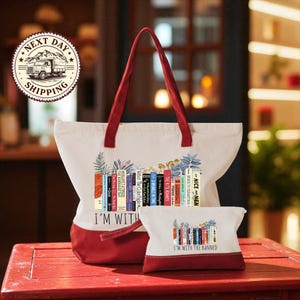A red and white tote bag with a printed design of colorful books, and a smaller white bag with a similar design, both placed on a red wooden surface.