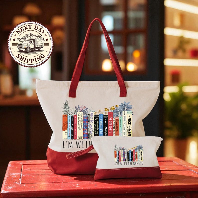 A red and white tote bag with a printed design of colorful books, and a smaller white bag with a similar design, both placed on a red wooden surface.