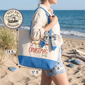 A woman carrying a large tote bag with a printed design on it, standing on a beach near the ocean.