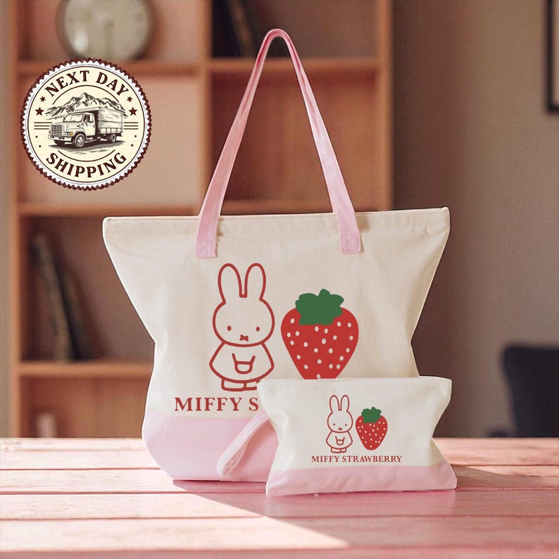 A pink tote bag with a cartoon rabbit and a strawberry on it, along with a smaller bag, is displayed on a wooden surface.