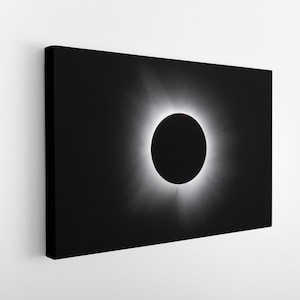 Può includere: Una fotografia in bianco e nero di un'eclissi solare. Il sole è completamente oscurato dalla luna, creando un anello di luce attorno alla sagoma scura.