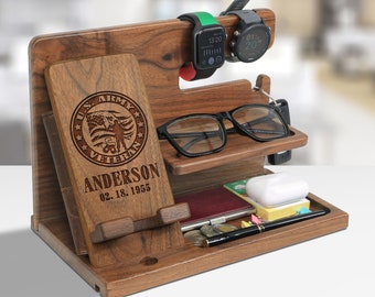 May include: A wooden phone and watch stand with a personalized inscription that reads "US Army Veteran Anderson 02.18.1955". The stand has a slot for a phone, a watch holder, a glasses holder, and a small tray for other items.