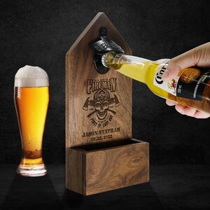 May include: Wooden wall mounted bottle opener with a firefighter theme. It features a skull with crossed axes and the text "This man is a Fireman, First in Last Out". The opener has a space for storing bottle caps. The text "Jason Statham 02.22.2022" is engraved below the design.