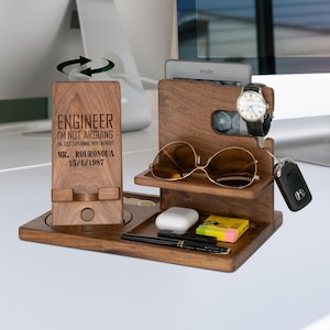 May include: A wooden desk organizer with multiple compartments. It holds a phone, sunglasses, a watch, keys, a Kindle, and other small items. The phone stand has the text "ENGINEER I'M NOT ARGUING I'M JUST EXPLAINING WHY I'M RIGHT MR. ROURONOUA 15/1/1987".