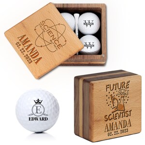 May include: A wooden box with a lid containing four golf balls. The lid is engraved with the text "SCIENCE IT'S LIKE BUT REAL" and the name "AMANDA" with the date "02.22.2023". The golf balls are engraved with the name "WILLIAM". The box is also engraved with the text "FUTURE SCIENTIST AMANDA 02.22.2023".