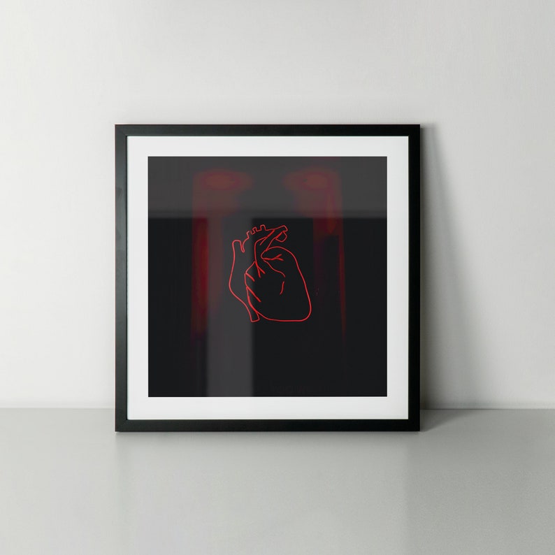 May include: Framed art print featuring a minimalist red outline of a human heart on a black background. The artwork is encased in a black frame with a white mat, creating a striking contrast. The overall aesthetic is modern and artistic.