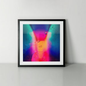 May include: Abstract art print in a black frame. The artwork features a vibrant, colorful design with a mix of pink, orange, blue, and teal hues. The image has a fluid, liquid-like appearance with bubble-like shapes.