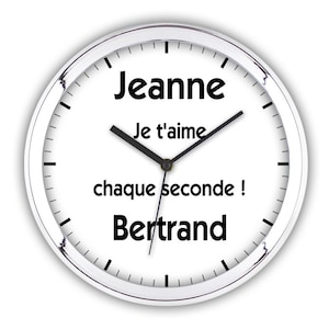 Peut inclure: Une horloge blanche avec des aiguilles noires et du texte noir qui dit "Jeanne Je t'aime chaque seconde! Bertrand". L'horloge a une bordure argentée.