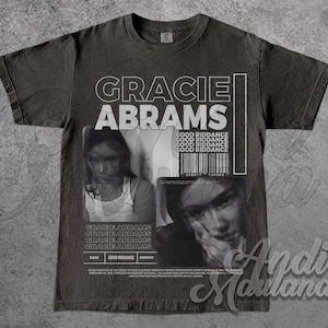Puede incluir: Camiseta gris oscuro con el texto "GRACIE ABRAMS" en blanco, junto con imágenes en blanco y negro de una mujer. La camiseta también incluye el texto "GOOD RIDDANCE" y un código de barras. La camiseta es merchandising del álbum "GOOD RIDDANCE".