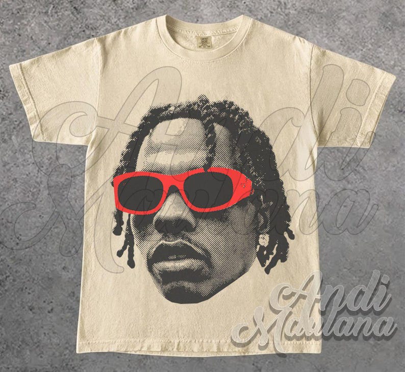 May include: Cream-colored t-shirt featuring a halftone portrait of a person wearing red sunglasses. The graphic is in black and gray tones. The shirt has a crew neck and short sleeves.