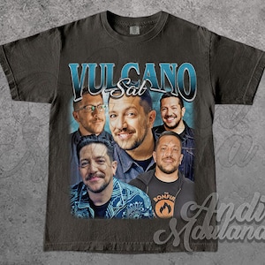 May include: Dark gray t-shirt featuring a collage of faces and the text "VULCANO Sat" in blue and white. The shirt has a vintage, distressed look, with a faded graphic design. The shirt is made of a soft material.