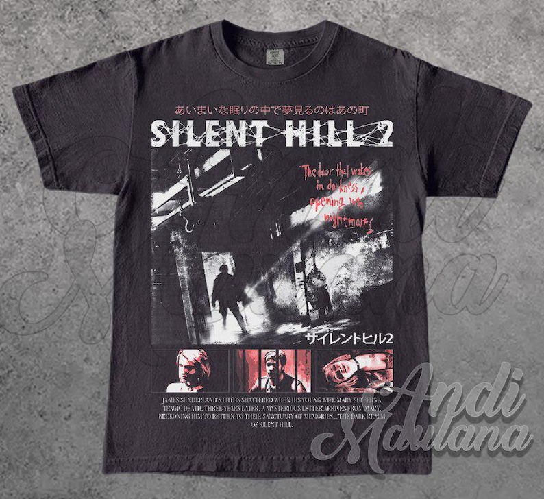 May include: Dark gray t-shirt featuring a graphic from Silent Hill 2. The design includes Japanese text, the game's title, and imagery of figures in a dark, urban setting. The shirt also has text that reads "The door that wakes in darkness, opening nightmare."