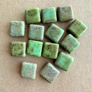May include: A collection of square, light green beads with a slightly weathered appearance. The beads are arranged on a light brown surface, showcasing their unique color variations and textures. Ideal for jewelry making.