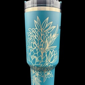 Peut inclure: Un gobelet en acier inoxydable bleu turquoise avec un motif floral dor&eacute;. Le gobelet est dot&eacute; d'un couvercle et d'une paille.