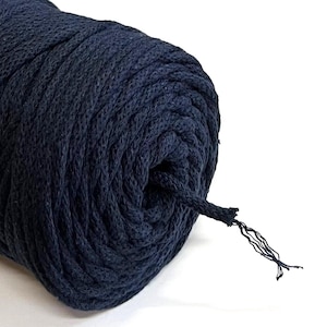 May include: A close-up of a dark navy blue spool of cotton rope. The rope is tightly wound, with a frayed end showing the individual fibers. The background is plain white.