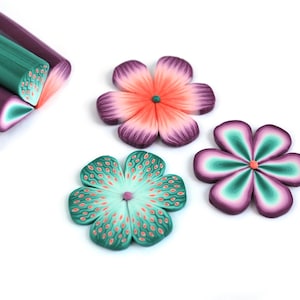 May include: Three polymer clay flowers in shades of green, pink, and purple. The flowers have a five-petal design and are handmade.