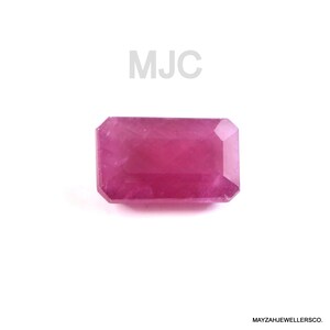 May include: A rectangular, faceted, pink gemstone with the text "MJC" above it. The gemstone is a vibrant shade of pink, with a polished surface. The bottom right corner of the image contains the text "MAYZAHJEWELLERSCO."